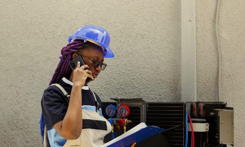 African american apprentice informing master technician over the phone about air conditioner parts needing to be replaced. Mechanic checking maintenance plan after finishing air filters cleaning